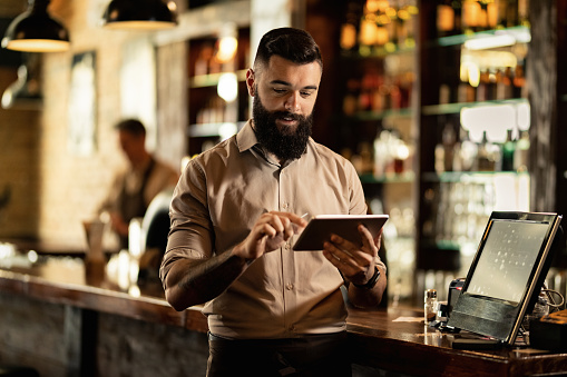 Young smiling waiter using touchpad while working in a pub.